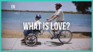 A man riding a bike while pulling a child in a trailer by a serene lakeside, with the text "What is Love?" above.