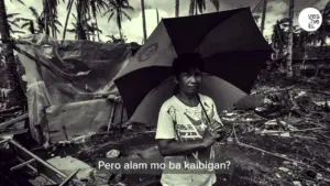 Young person with an umbrella stands in a devastated area, surrounded by debris and palm trees, conveying resilience amidst disaster.