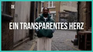 Man in a green jacket standing in a cobblestone alleyway with the text "Ein Transparentes Herz" above him.