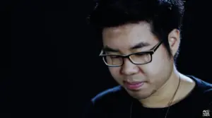 Young man with glasses looking down thoughtfully against a dark background, showcasing a moment of reflection.