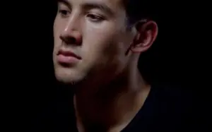 Close-up of a thoughtful young man in dim lighting, showcasing his focused expression and facial contours.