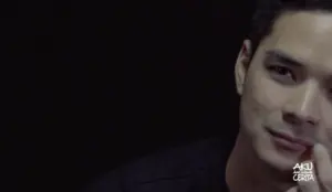 Close-up of a contemplative young man with a slight smile against a dark background, exuding charm and intrigue.