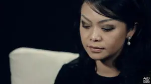 Close-up of a woman with elegant makeup and earrings, gazing thoughtfully while seated against a dark background.