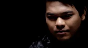 Close-up portrait of a young man with intense expression against a dark background, highlighting his features and mood.