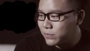 Young man with glasses in a contemplative expression, set against a soft-focus background.