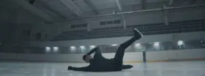 A figure skater performs a dramatic fall on an empty ice rink, showcasing athletic grace and determination in motion.