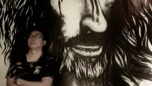 Person standing beside a large, detailed black-and-white mural of a bearded face, showcasing intricate artistic expression.