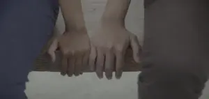 Two hands of different skin tones clasping a wooden bar, symbolizing unity and connection.