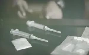 Two syringes and a small packet on a table, suggesting a medical or pharmacological setting.