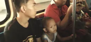 A young boy and toddler sit quietly on public transport, engaging with their surroundings.