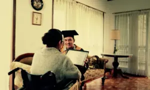 A graduate proudly shows their diploma to a family member in a cozy living room setting.