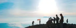 Hikers at a mountain summit with a flag against a bright sky, capturing a moment of adventure and achievement.