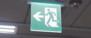 Green exit sign with a running figure and left arrow, indicating the emergency exit path in a building.