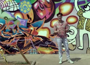 Person standing in front of a vibrant graffiti mural with colorful patterns and designs.