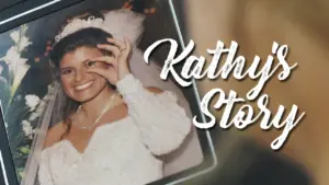 Bridal portrait of Kathy smiling in a wedding dress, holding her hand near her face, with a floral background.