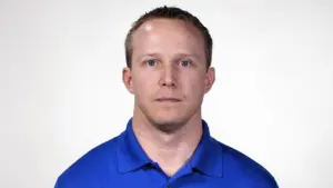 Professional headshot of a man with short hair wearing a blue polo shirt, looking directly at the camera with a neutral expression.