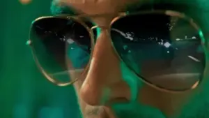 Close-up of a person wearing reflective sunglasses, with vibrant green lighting in the background.