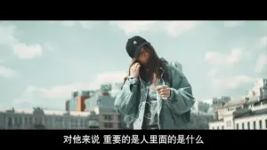 Young woman in oversized denim jacket and cap, standing outdoors, holding a drink, with a city skyline in the background.