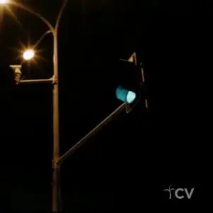 Traffic light glowing green at night with street lamps illuminating the scene, showcasing a quiet urban intersection.