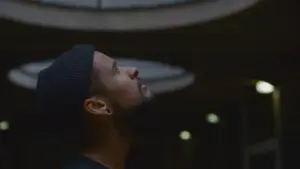 Man gazing upward in a dimly lit space, illuminated by a circular skylight above.