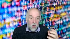 Person speaking in front of a vibrant, colorful digital background filled with binary code and data patterns.