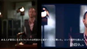 A man speaks on camera in a professional setting, with a blurred background and text in Japanese displayed on the screen.