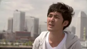 Young man with tousled hair gazes thoughtfully at the skyline, featuring modern buildings under a bright sky.