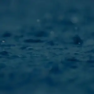 Close-up of raindrops splashing on a dark surface, creating a serene and calming atmosphere.