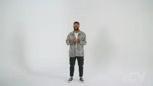 Man wearing a striped jacket and sneakers standing confidently against a plain white background.