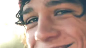 Close-up of a young man's smiling face, capturing bright eyes and a cheerful expression in natural daylight.