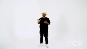 Person in a black shirt and hat gesturing against a minimalist white background. Casual style and expressive pose.