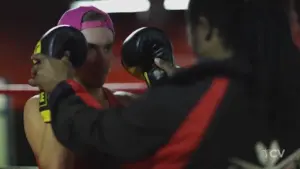 Male boxer in a pink cap trains with a coach, focusing on technique with boxing pads in a gym setting.