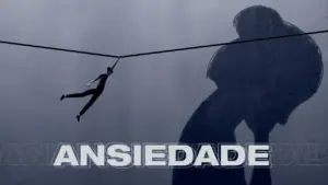 A person balancing on a tightrope casts a large shadow, with the word "ANSIEDADE" prominently displayed below.