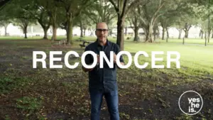 Man standing in a park with trees, holding a sign that says "RECONOCER" against a calm, natural backdrop.