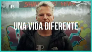 Man in a black jacket stands against a colorful graffiti backdrop with the text "Una vida diferente" above him.