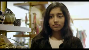 Young woman standing in a boutique surrounded by unique decor items, looking thoughtfully at the camera.