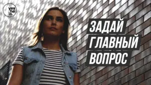 Young woman in a striped shirt and denim vest standing against a textured wall with bold text in Russian.