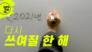 Hand writing the year 2021 on a gray surface, bold text encourages renewed writing efforts in Korean.