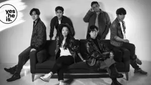 A diverse group of six stylish individuals pose together on a couch, showcasing modern fashion in a black-and-white setting.