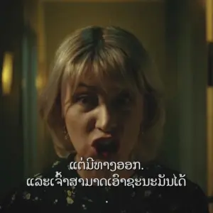 A woman with short blonde hair passionately speaking in a dimly lit hallway, conveying strong emotions.