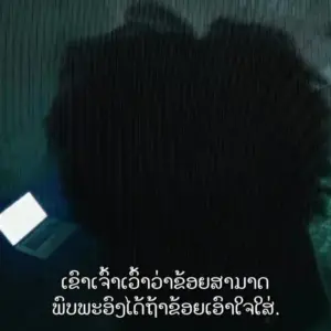 Silhouette of a person with curly hair using a laptop in a dark setting, with text in an Asian language below.