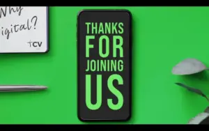 A smartphone on a green background displaying "Thanks For Joining Us" with a notepad and pen nearby.