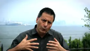 A man gesturing passionately with a bay view in the background, conveying an engaging message outdoors.