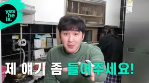 A man gesturing enthusiastically in a kitchen, encouraging viewers to listen closely to his story.