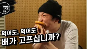 Man in a beanie humorously bites into food, with Korean text questioning hunger. Fun and engaging food scene.