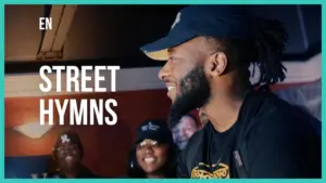 Smiling performer wearing a cap, engaging audience at a vibrant live event labeled "Street Hymns."