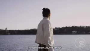 Person wearing a jacket standing by a serene lake, gazing into the distance, with a peaceful sky above.