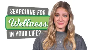 A smiling woman in a gray sweater alongside the text "Searching for Wellness in Your Life?" on a bright background.