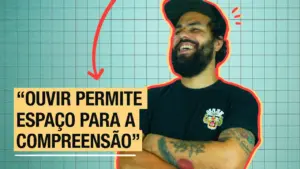 Man with a beard smiling, wearing a black shirt with a quote about listening and understanding on a grid background.