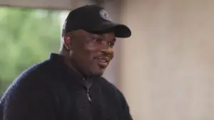 Smiling man wearing a black cap, sitting indoors with a soft focus background, exuding warmth and approachability.